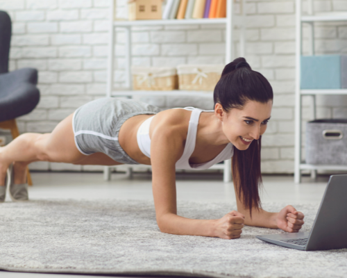 Woman doing ab workout at home on carpet looking at laptop