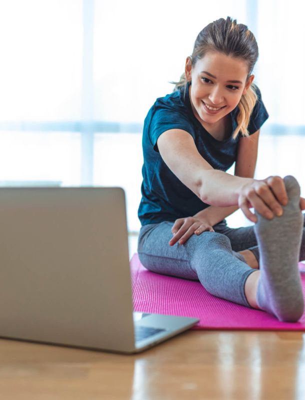 woman looking at laptop doing stretching on pink mat in living room