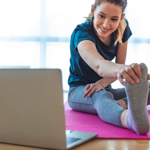woman looking at laptop doing stretching on pink mat in living room